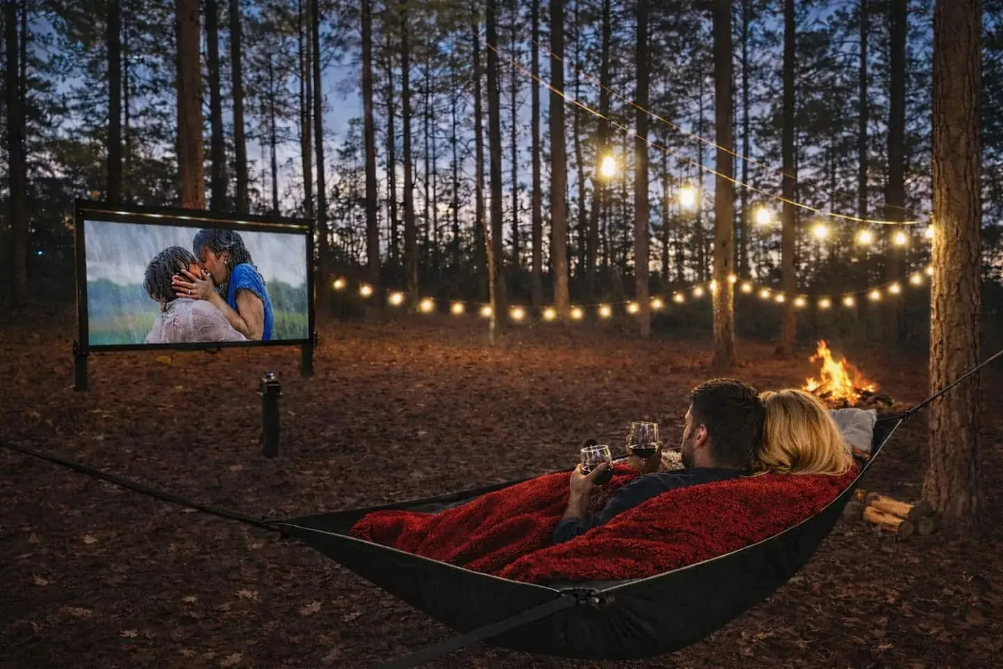 A couple sharing wine in the outdoor hammock while watching a movie beneath the string lights