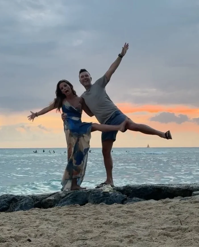 Amy and Karl striking a playful pose together by the ocean at sunset